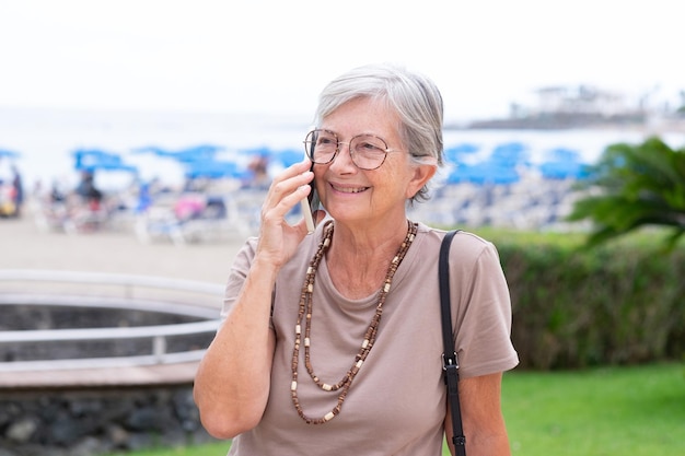 Ritratto di donna anziana caucasica seduta all'aperto in una giornata nuvolosa estiva utilizzando il telefono cellulare attraente femmina sorridente godendo relax e vacanza