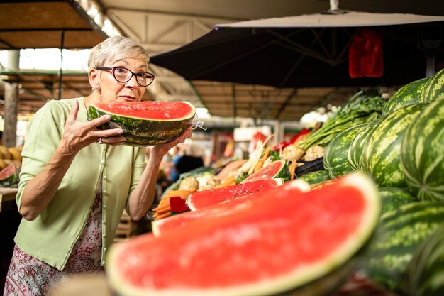 Ritratto di donna anziana che acquista anguria organica fresca al mercato per un nutrimento sano.