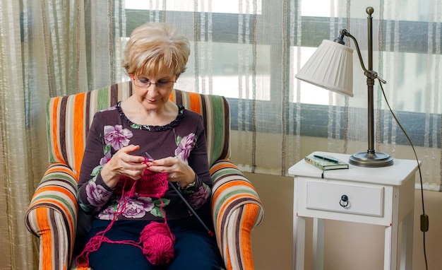 Ritratto di donna anziana che lavora a maglia un maglione di lana a casa