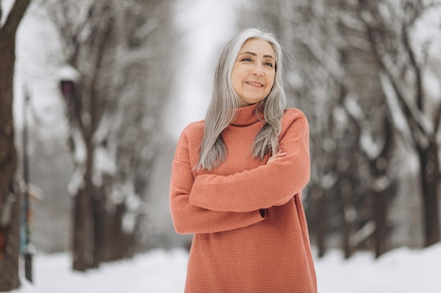 Ritratto di donna anziana con i capelli grigi in maglione lavorato a maglia sorridente sullo sfondo in inverno