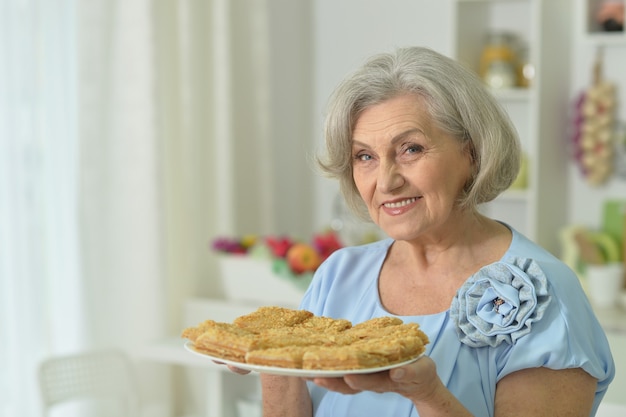 Ritratto di donna anziana felice con una gustosa torta a casa