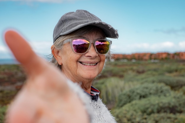 Ritratto di donna anziana felice in occhiali riflettenti e cappello durante un'escursione all'aperto guardando la fotocamera