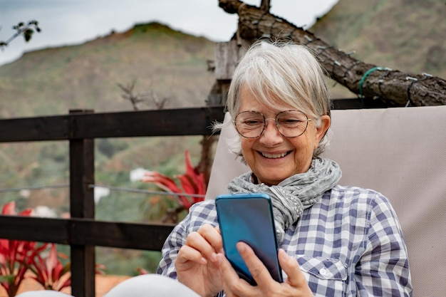 Ritratto di donna anziana seduta all'aperto in giardino durante l'utilizzo del telefono Donna sorridente matura scrivendo un messaggio sul suo cellulare