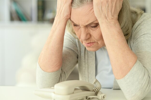 Ritratto di donna anziana triste a casa con il telefono