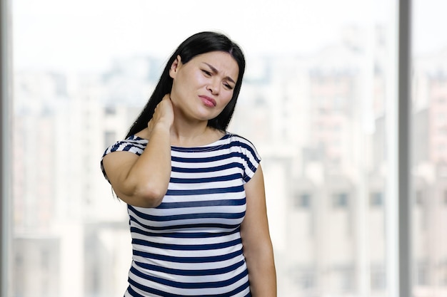 Ritratto di donna asiatica che soffre di dolore al collo sfondo delle finestre dell'ufficio