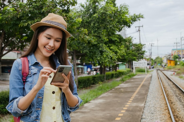 Ritratto di donna asiatica che trasporta zaino e guarda il suo smartphone pronto per andare in vacanza.