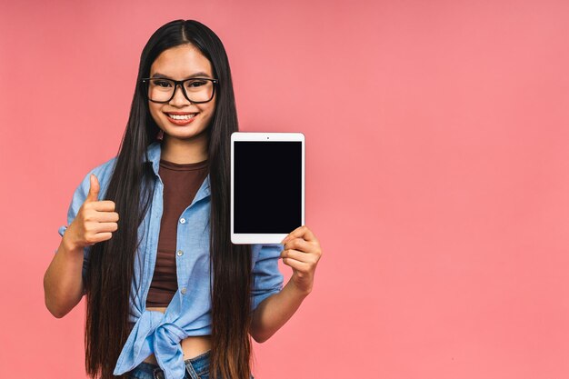 Ritratto di donna asiatica felice sorridente che mostra o presenta computer tablet isolato su sfondo rosa