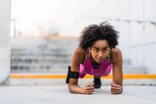 Ritratto di donna atleta afro facendo flessioni sul pavimento all'aperto. Sport e concetto di stile di vita sano.