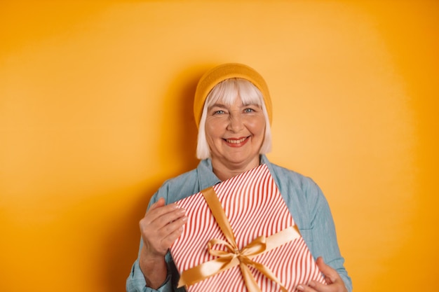 Ritratto di donna attraente e divertente 40s 50s mani in possesso di confezione regalo su sfondo di colore arancione brillante. Vacanze di Natale, presente, concetto di felicità