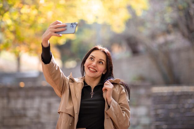 Ritratto di donna attraente ed elegante nella stagione autunnale con trench sta prendendo un selfie