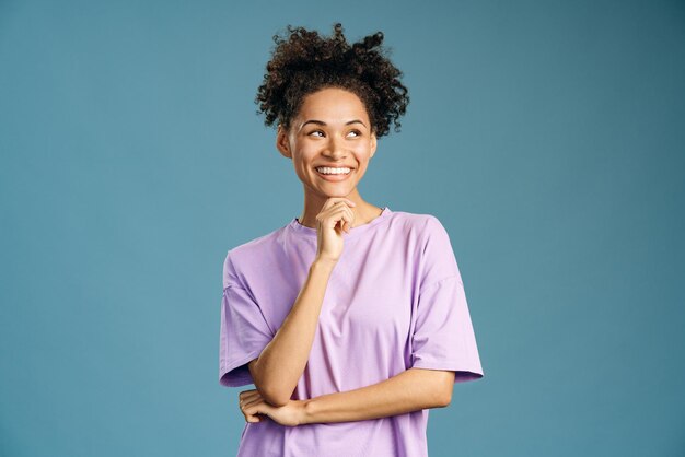 Ritratto di donna attraente in piedi e distoglie lo sguardo con un sorriso a trentadue denti isolato su sfondo blu. Concetto di donna sicura