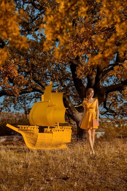 Ritratto di donna bella rossa con libro e nave vicino alla quercia in autunno