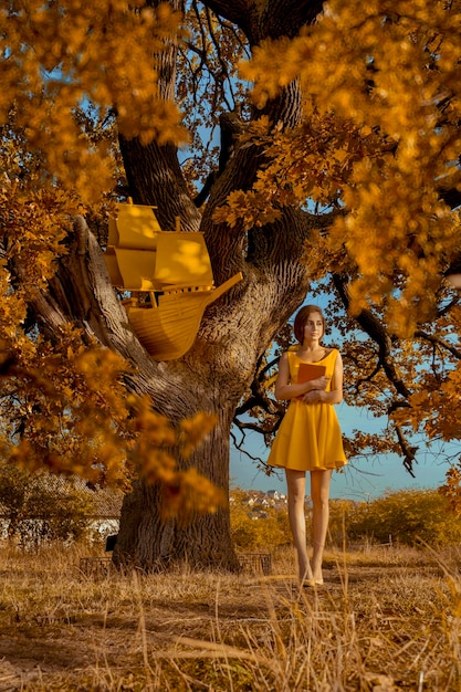 Ritratto di donna bella rossa con libro e nave vicino alla quercia in autunno