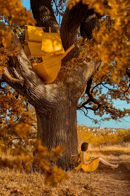 Ritratto di donna bella rossa con libro e nave vicino alla quercia in autunno