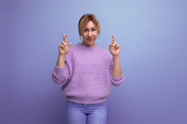 Ritratto di donna bionda carina adorabile sognante e speranzosa in maglione casual con le braccia incrociate su viola