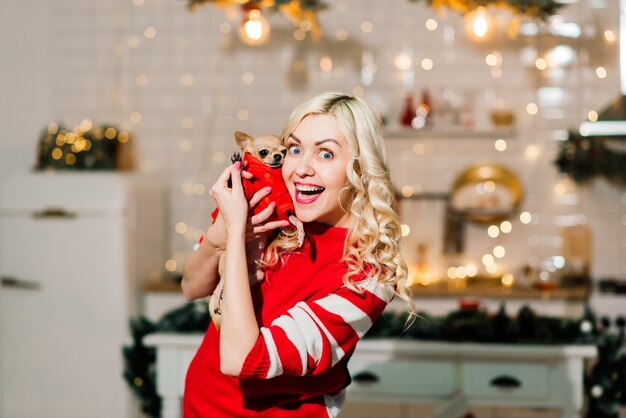 Ritratto di donna bionda che indossa il Natale Santa tenendo il cane chihuahua