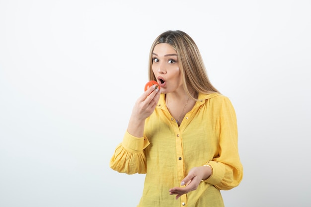 Ritratto di donna bionda che mangia pomodoro rosso lucido