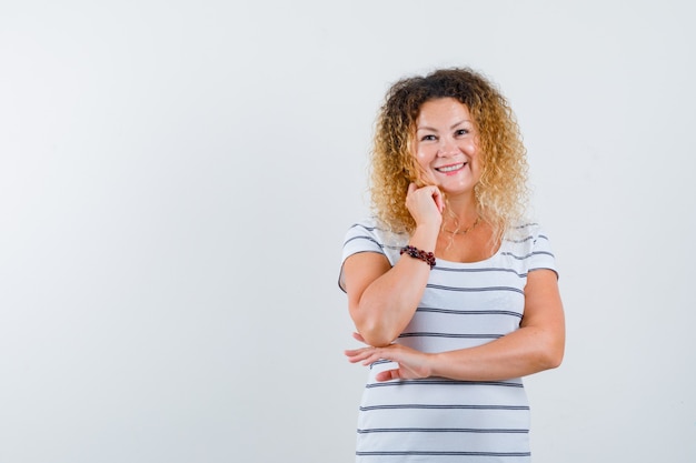 Ritratto di donna bionda che puntella il mento in mano con una maglietta a righe e sembra allegra vista frontale