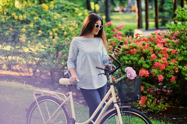 Ritratto di donna bruna attraente con bicicletta da città in un parco all'aperto estivo.