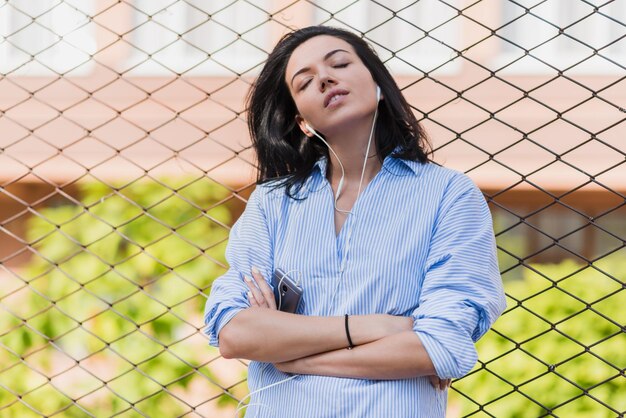 Ritratto di donna bruna attraente con godersi il tempo ascoltando musica e aspettando un amico sulla strada della città Giovane donna d'affari pensierosa bruna che tiene smart phone e ascolta la musica