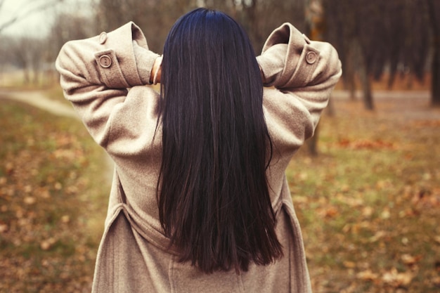 Ritratto di donna bruna capelli in cappotto beige che cammina al parco della città