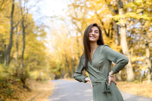 Ritratto di donna bruna in abito verde in posa in autunno park