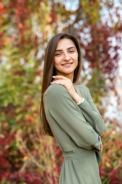 Ritratto di donna bruna in abito verde in posa in autunno park