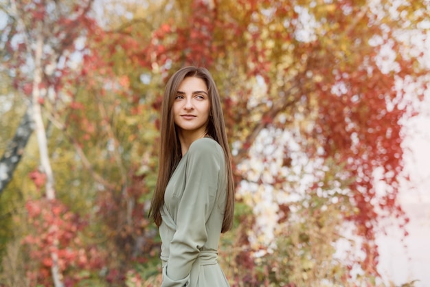 Ritratto di donna bruna in abito verde in posa nella sosta di autunno