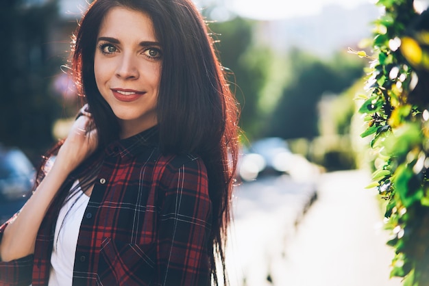 ritratto di donna bruna positiva vestita con una camicia elegante che trascorre il tempo libero in una strada soleggiata