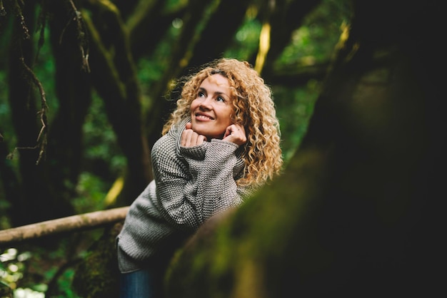 Ritratto di donna caucasica attraente che sorride e si gode la foresta di boschi verdi all'aperto. Persone e viaggi di stile di vita ambientale della natura. Bel sorriso femminile sdraiato su un tronco d'albero