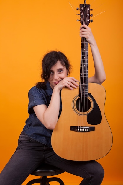 Ritratto di donna caucasica con la sua chitarra acustica in studio su sfondo giallo. Signora allegra con uno strumento musicale.