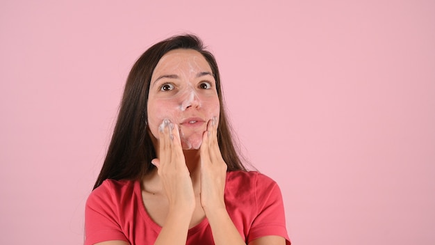 Ritratto di donna che pulisce il viso con un trattamento in schiuma sul rosa