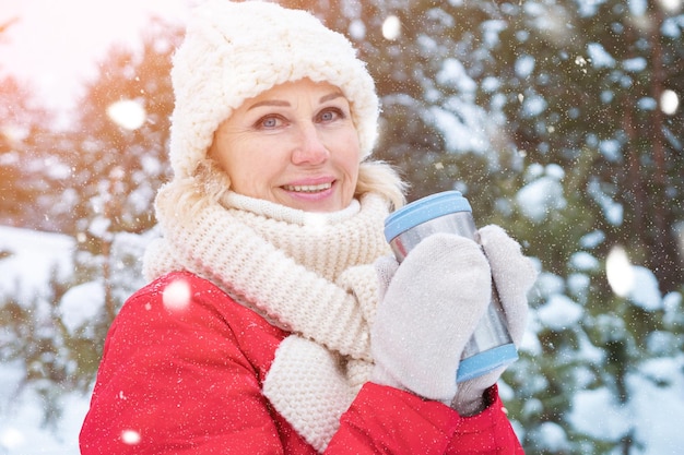 Ritratto di donna che tiene una tazza termica nella foresta invernale innevata