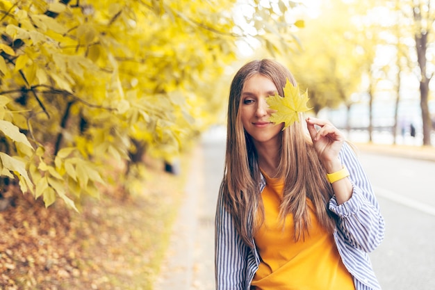 Ritratto di donna con foglia d'acero gialla autunnale vicino