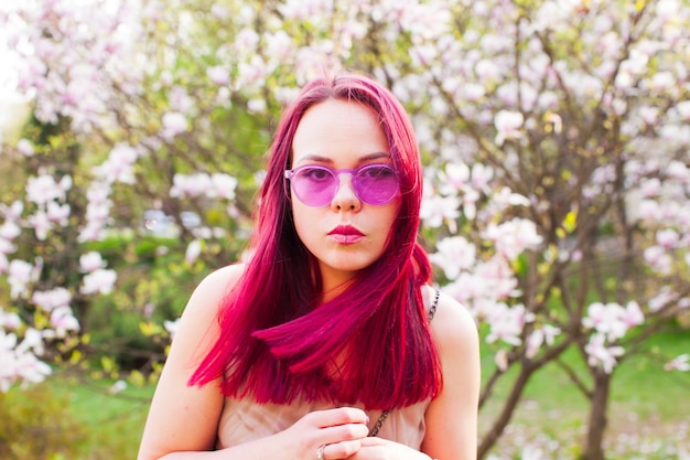 Ritratto di donna creativa attiva con capelli rosa e piercing. La donna sogna con gli occhiali rosa