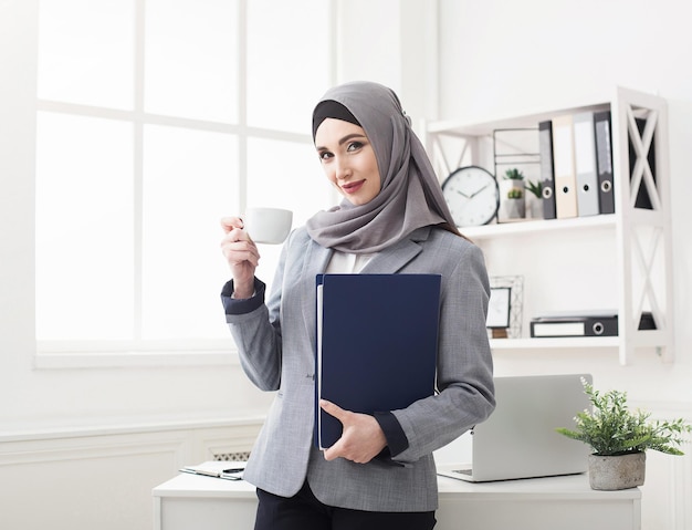 Ritratto di donna d'affari araba in ufficio. Ceo con cartellina e tazza di caffè