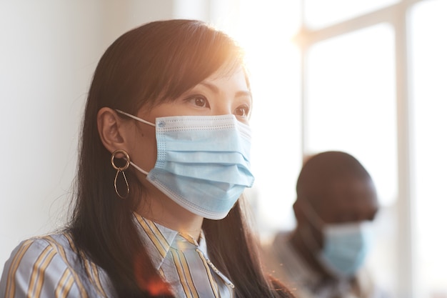 Ritratto di donna d'affari asiatica che indossa una maschera e guarda lontano mentre è seduta tra il pubblico alla conferenza di lavoro, copia spazio