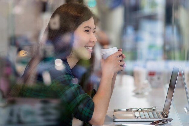 Ritratto di donna d'affari asiatica in abito casual che beve e lavora con un computer portatile tecnologico