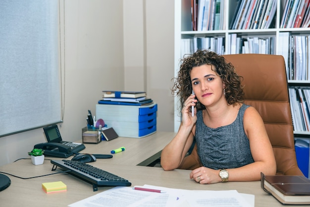 Ritratto di donna d'affari che guarda mentre parla con lo smartphone seduto in ufficio