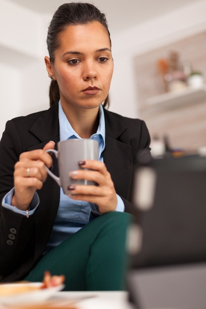 Ritratto di donna d'affari che guarda sul tablet e beve una tazza di caffè