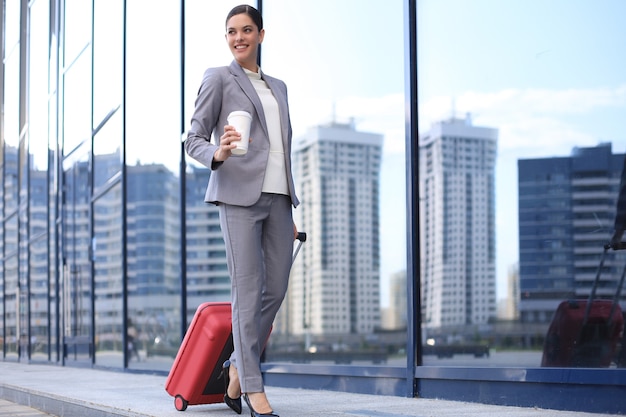 Ritratto di donna d'affari di successo che viaggia con custodia in aeroporto. Bellissimo viaggio femminile alla moda con i bagagli.