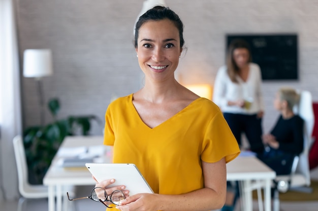 Ritratto di donna di affari abbastanza giovane che guarda l'obbiettivo. Sullo sfondo, i suoi colleghi che lavorano in ufficio.