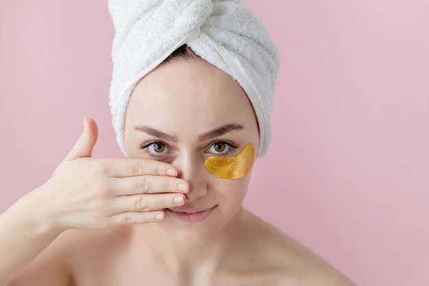 Ritratto di donna di bellezza con bende sugli occhi sulla parete rosa. Fronte di bellezza della donna con la maschera sotto gli occhi. Bella donna con trucco naturale e patch di collagene cosmetici d'oro sulla pelle del viso fresca.