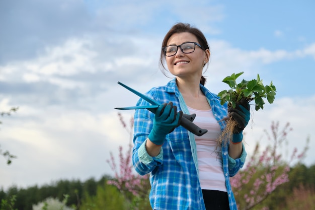 Ritratto di donna di mezza età in giardino con strumenti, cespugli di fragole