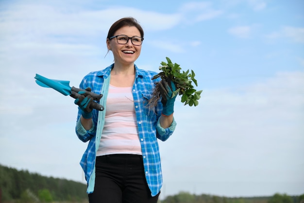 Ritratto di donna di mezza età in giardino con strumenti, cespugli di fragole