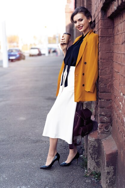 Ritratto di donna di moda che cammina per strada. Indossa una giacca gialla, sorridendo a lato.