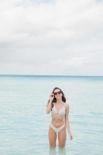 Ritratto di donna di moda sportiva piuttosto bella in bikini bianco in posa in estate vicino al mare