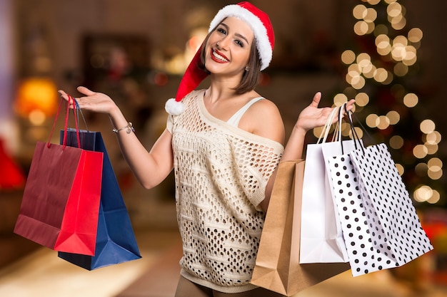 Ritratto di donna di Natale che tiene i sacchetti della spesa. Donna felice sorridente sopra le luci di Natale del bokeh