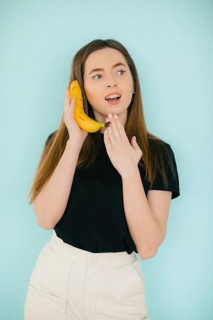 Ritratto di donna divertente che chiama un telefono banana su sfondo blu