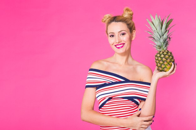 Ritratto di donna divertente e ananas sulla parete rosa con copyspace.